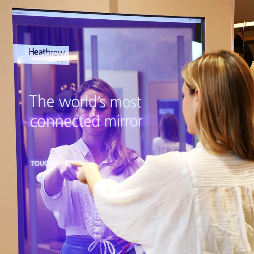 Shopper trying on clothes in front of a full-length digital mirror showing augmented reality effects on their reflection