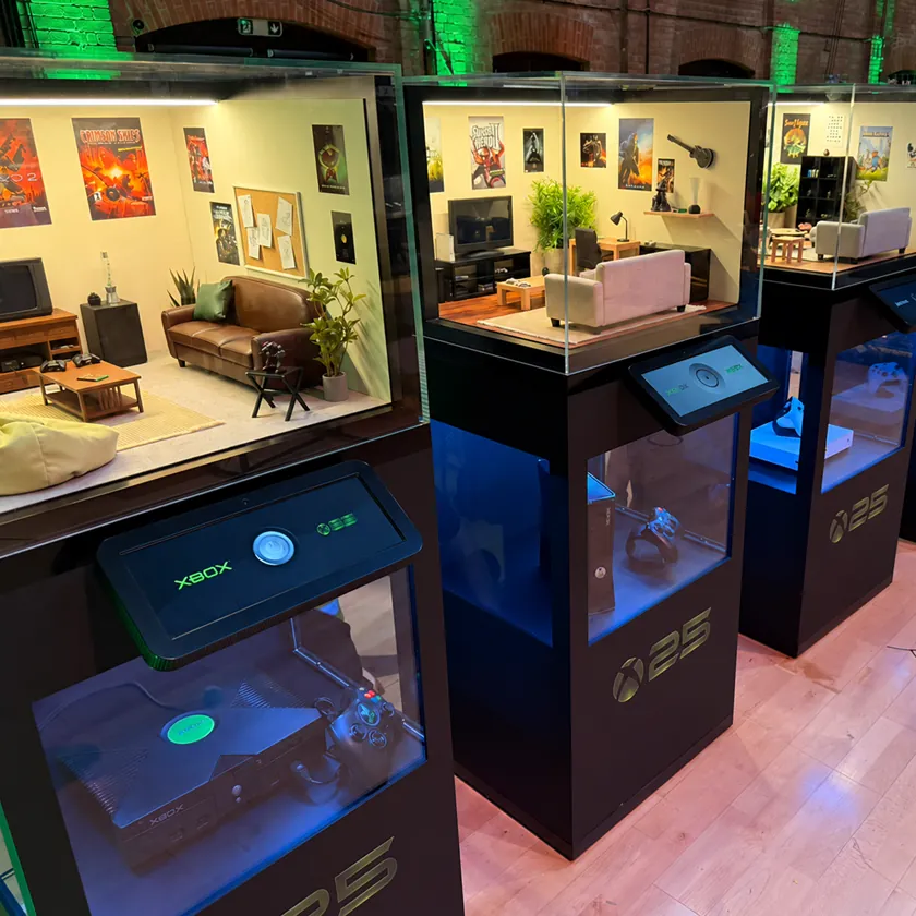 Row of display plinths each showing a games console above a miniature living room diorama from a different decade