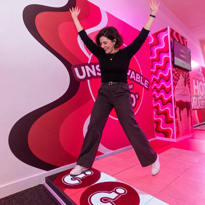 Person jumping between glowing tiles on an LED floor while onlookers watch from the edge of the game area