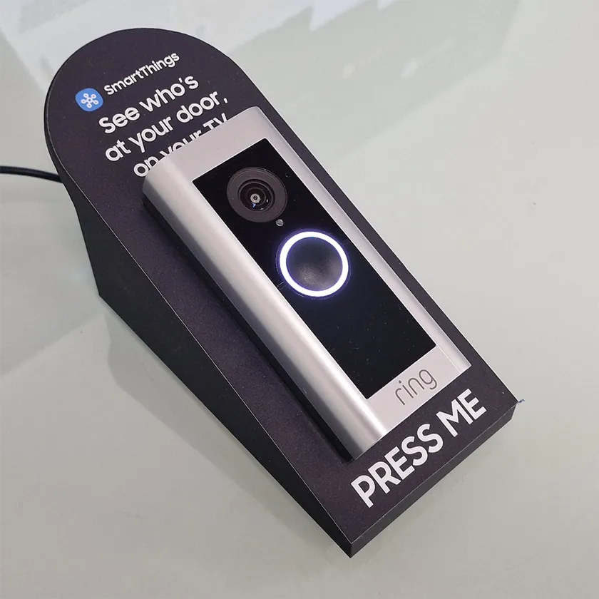 Shopper pressing a replica doorbell on a display beside a large TV showing a video of a parcel delivery